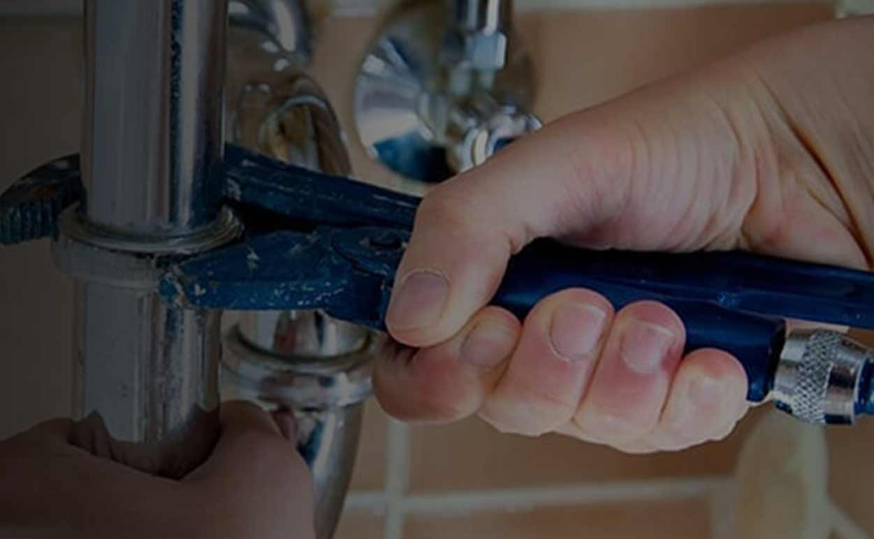 Plumber Tightening a Pipe With a Blue Wrench.